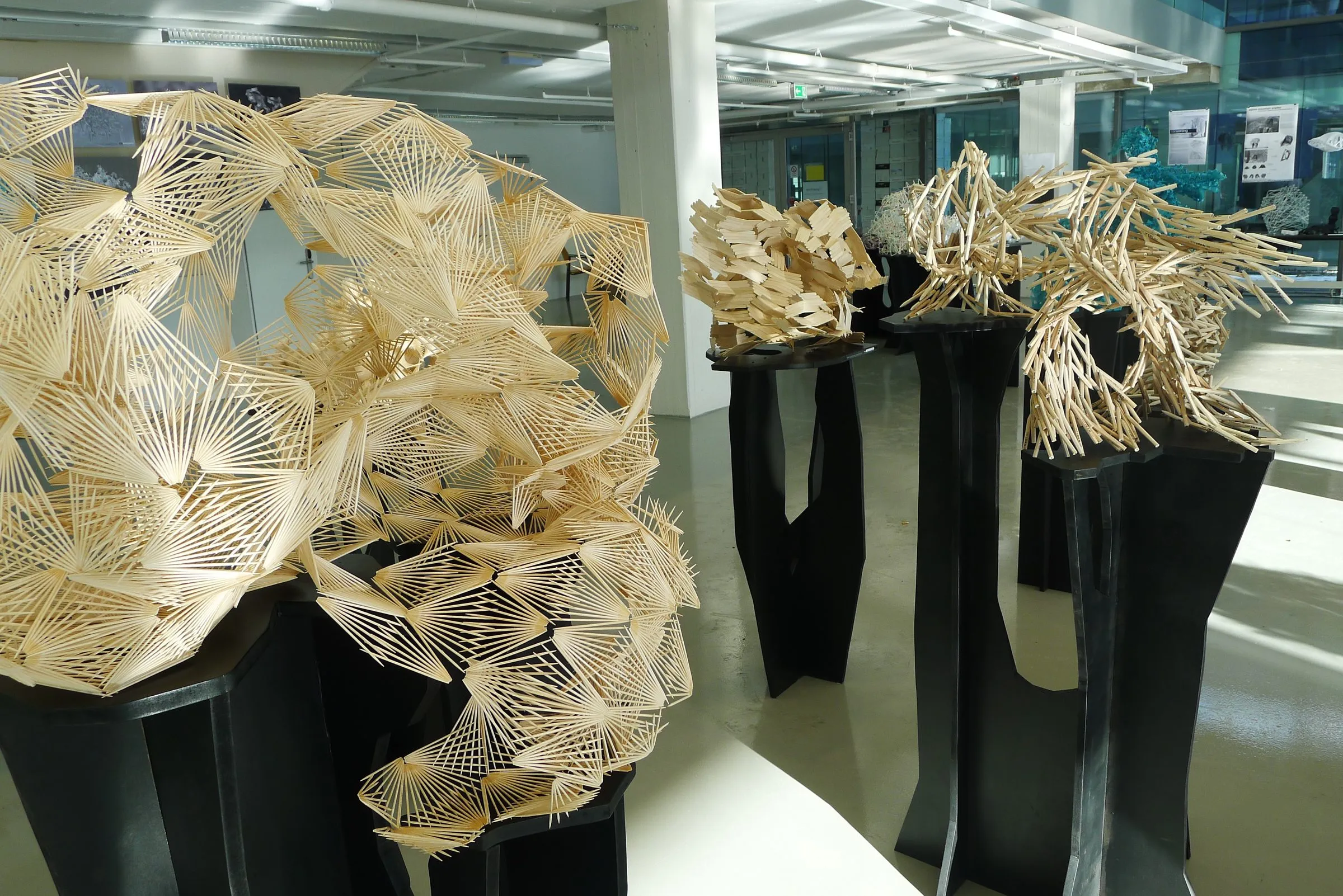 Aggregate models in card, wire, and paper displayed on black stands in a bright hall