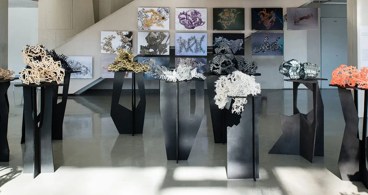 Coloured aggregate models on black stands in front of drawings pinned to a wall