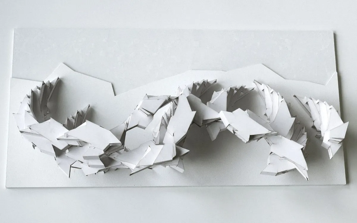 A white relief model of housing along a canal, its parts cut and folded from card, photographed from above