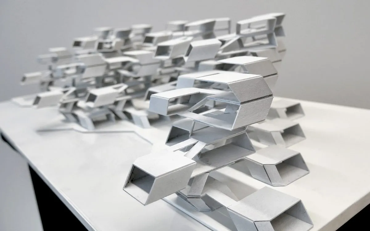 A white card model of stacked housing parts photographed on a table