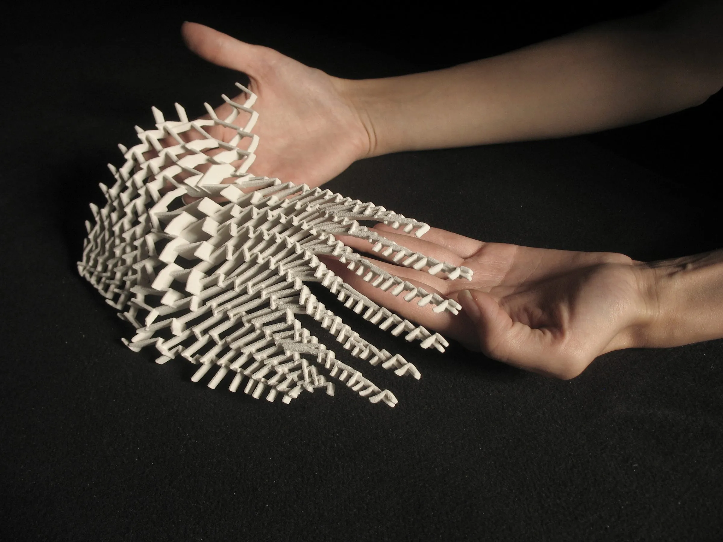 Two hands holding a small model of white folded paper elements aggregated into a curved cluster
