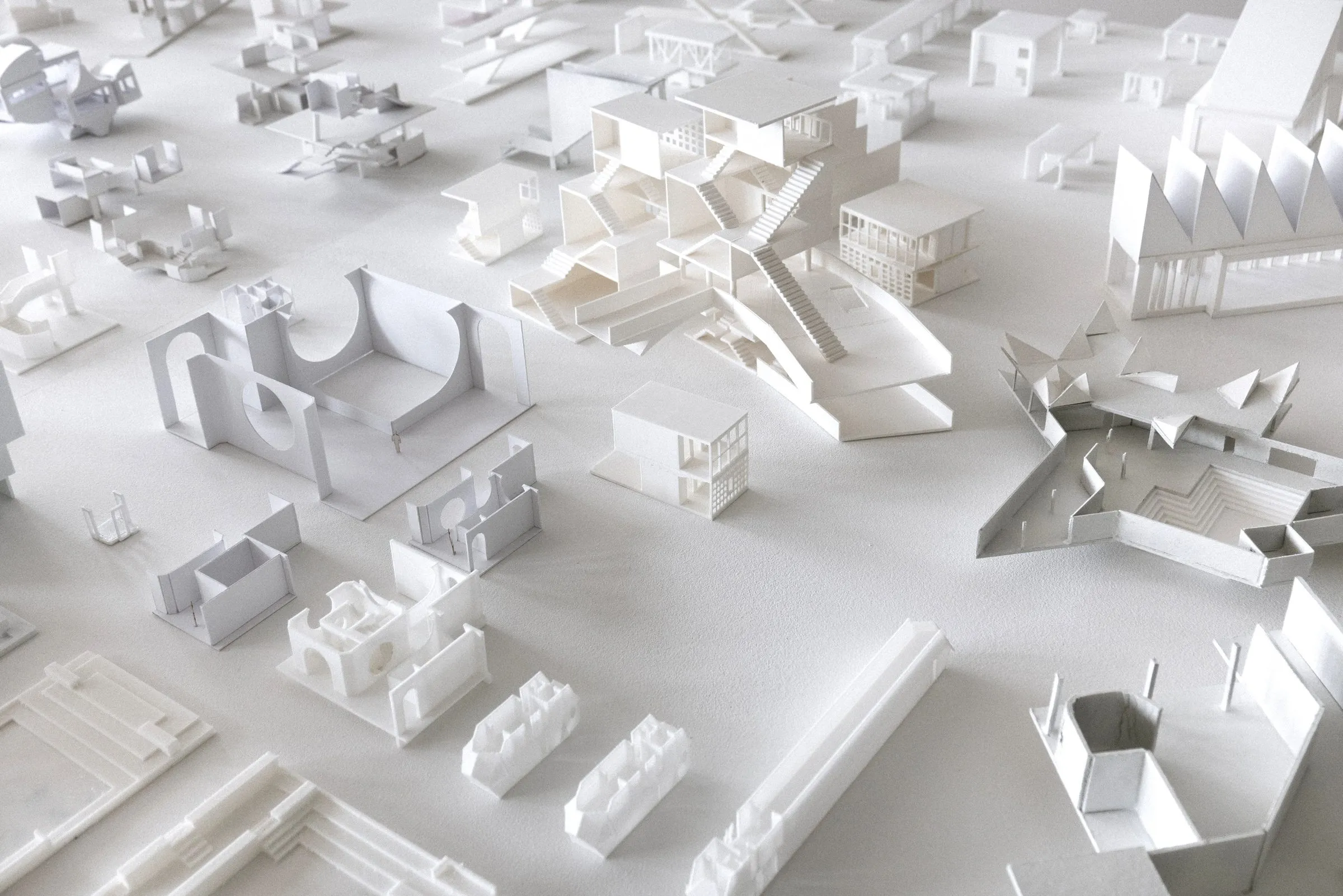 A field of small white student models on a white table, each a fragment of a building read as a city