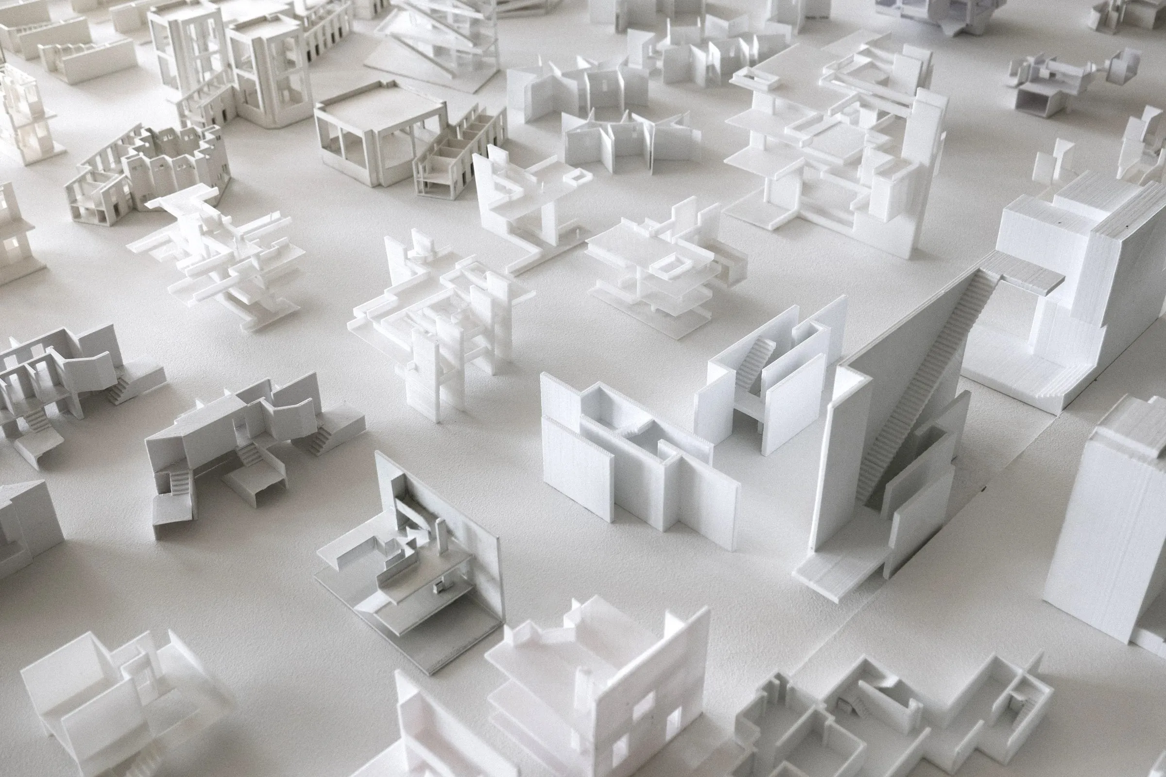 Close view of white models: a sawtooth roof, stacked terraces, a courtyard block