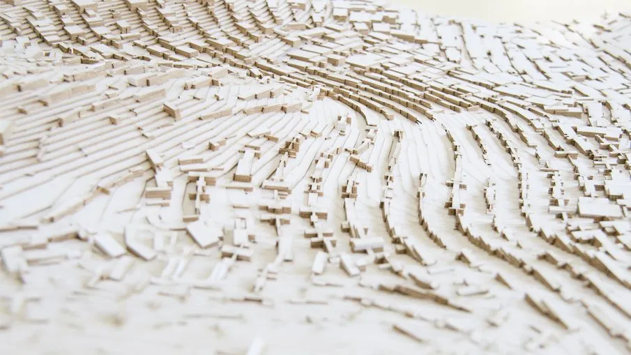 A white relief model in which rows of small blocks swell into a wave-like field