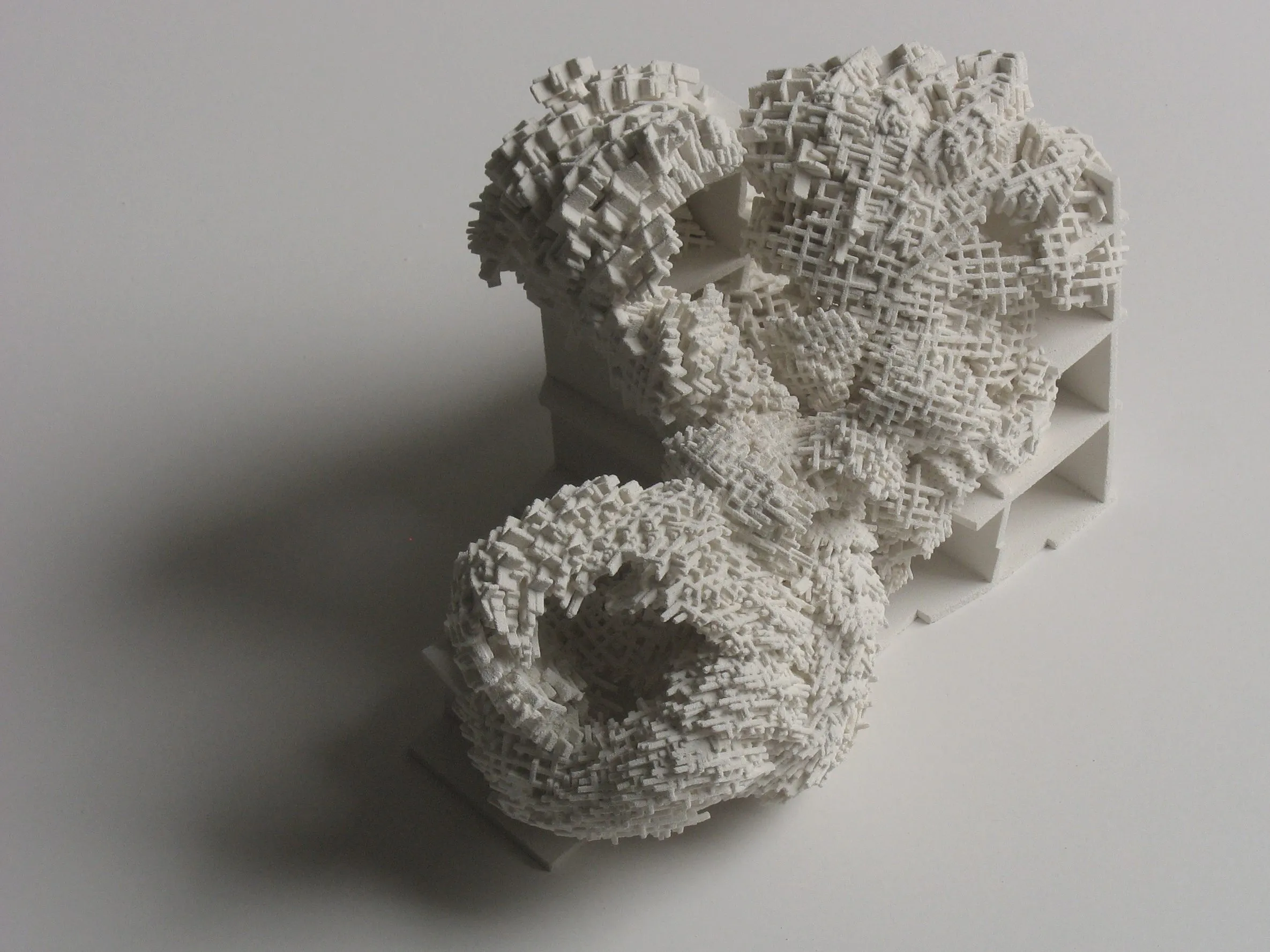 Photograph of a white model: a coral-like mass of cut flakes growing out of a grid of slabs and columns