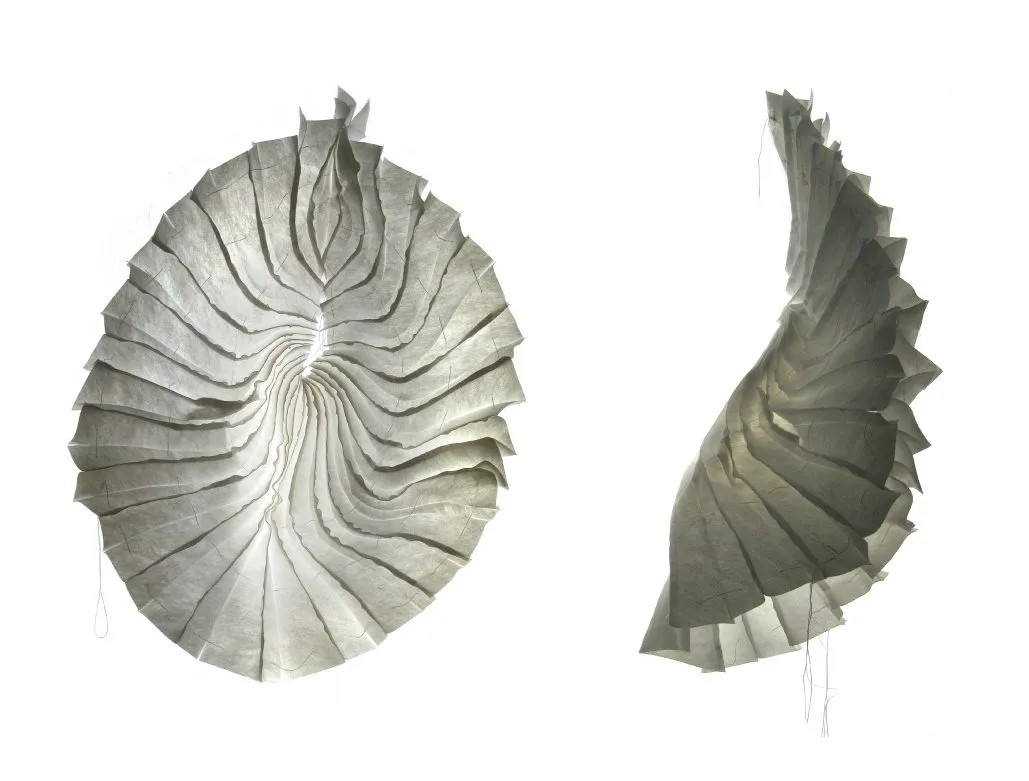 Photographs of a sewn object of pleated grey strips, once opened into a disc and once folded into a bag