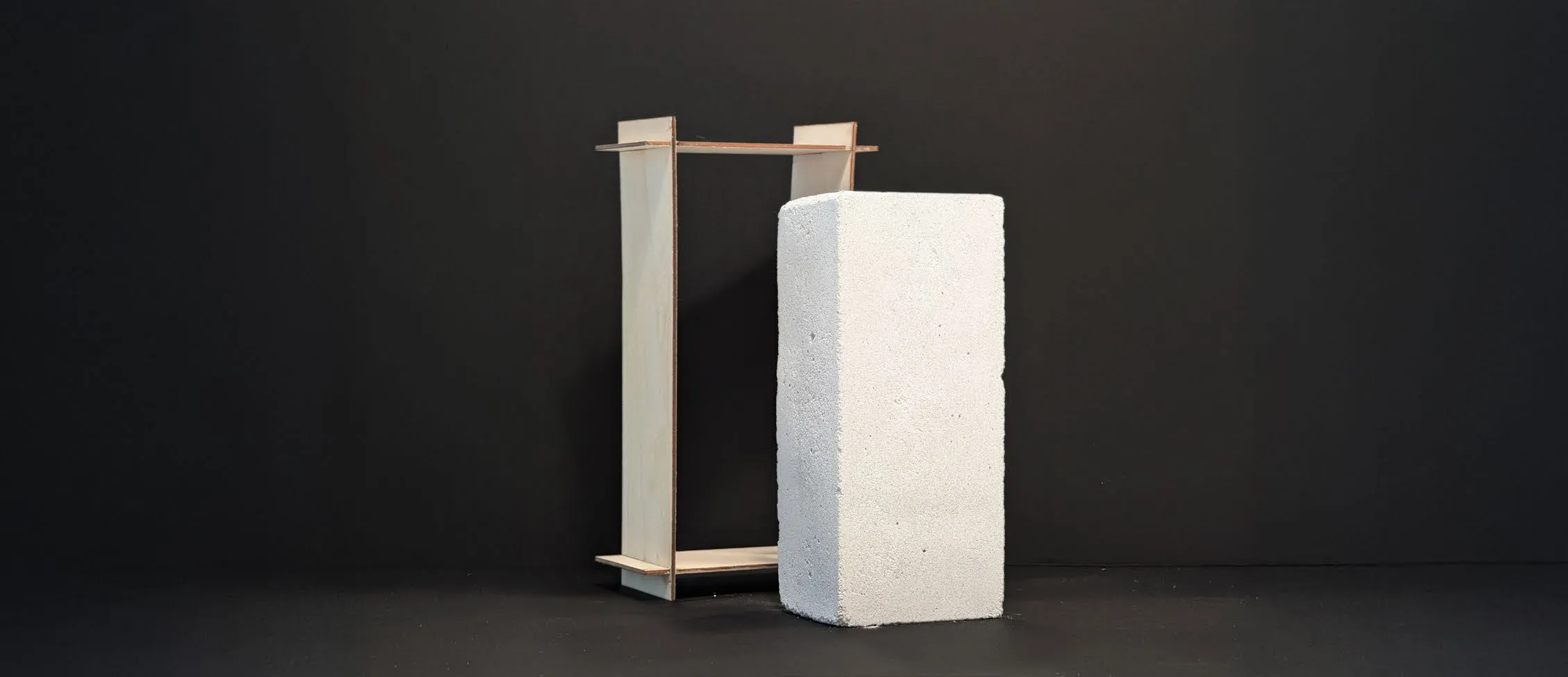 A pale, air-dried brick of a synthetic calcium silicate standing on a black table beside a small wooden frame
