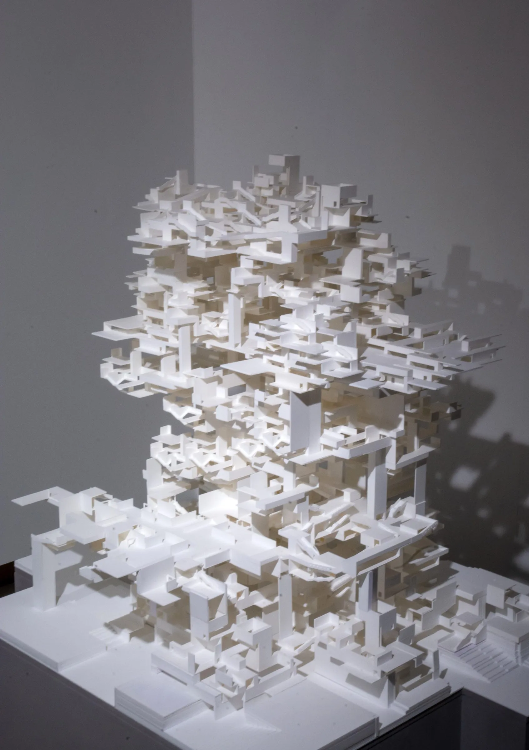 A white and tan model of nested rooms and passages stacked into a tower on a grey plinth