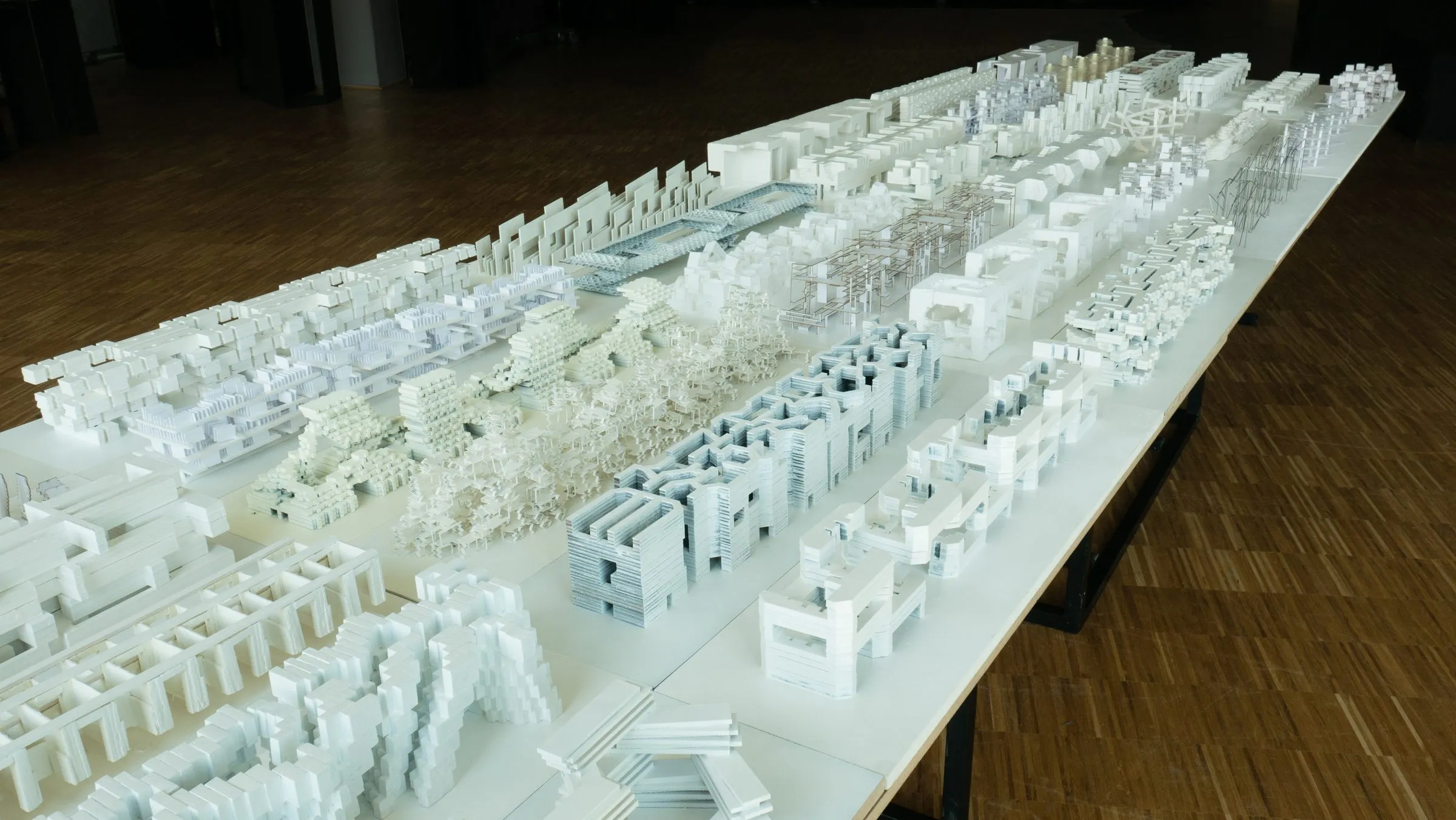 A long table of small white models, each a city configured as a slab