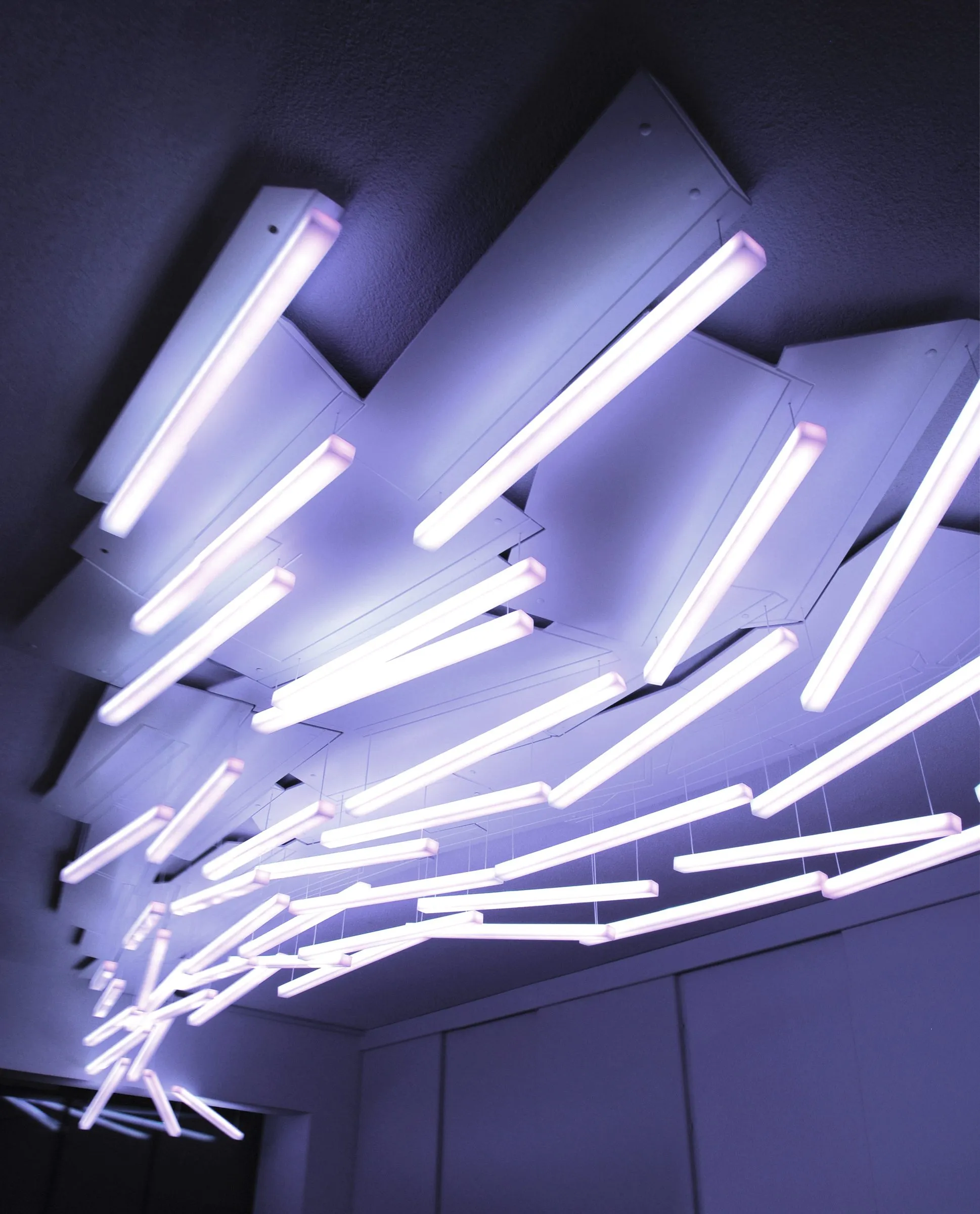 The white light poles seen from below, fanning out across the ceiling from the corner of the room, their light tinted violet