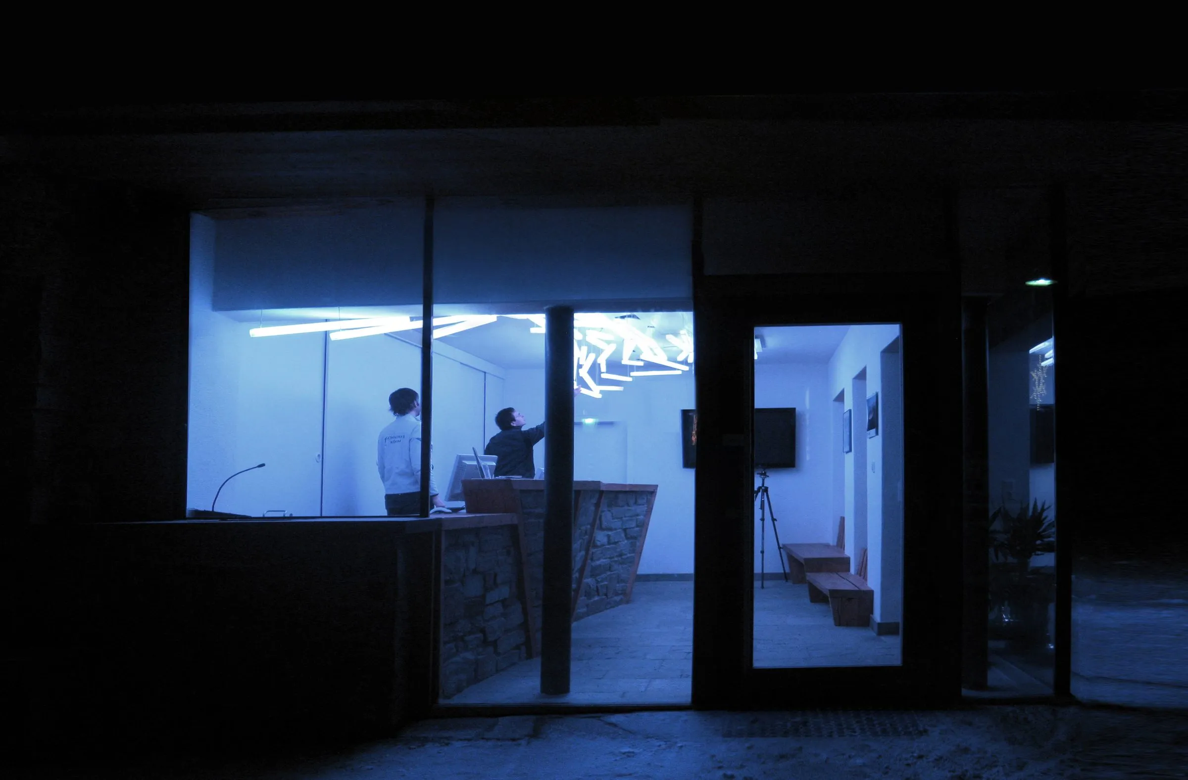 A cloud of white fluorescent light poles spreading across the ceiling of a white room, the light tinted violet