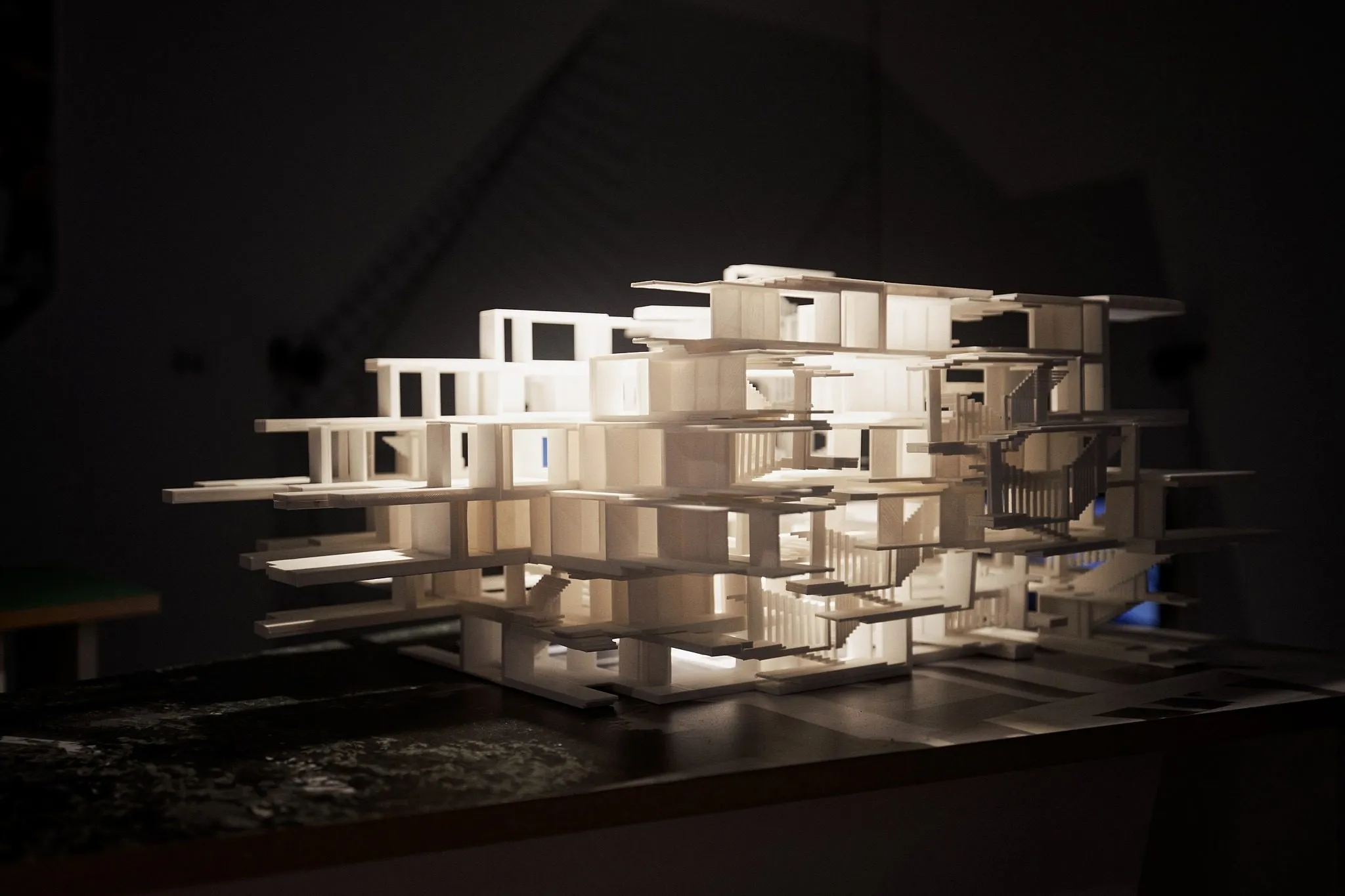 The white stacked model of Living with Trees lit from above in the dark exhibition room