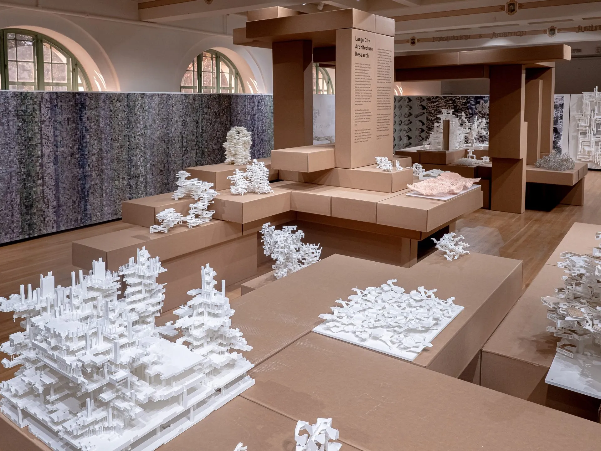 White models on cardboard platforms seen close, the printed wall and an arched window behind them