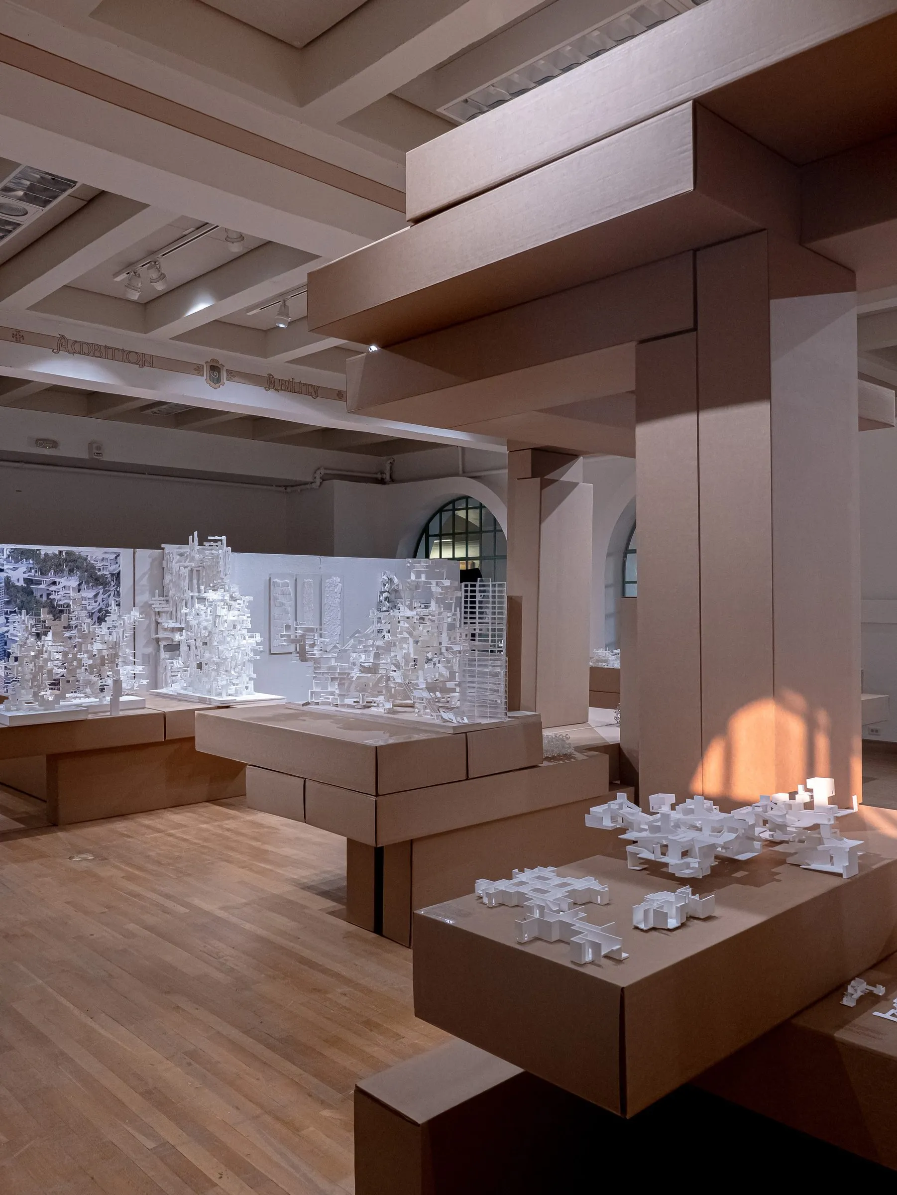 View through the cardboard beams to platforms of white models and the printed wall behind