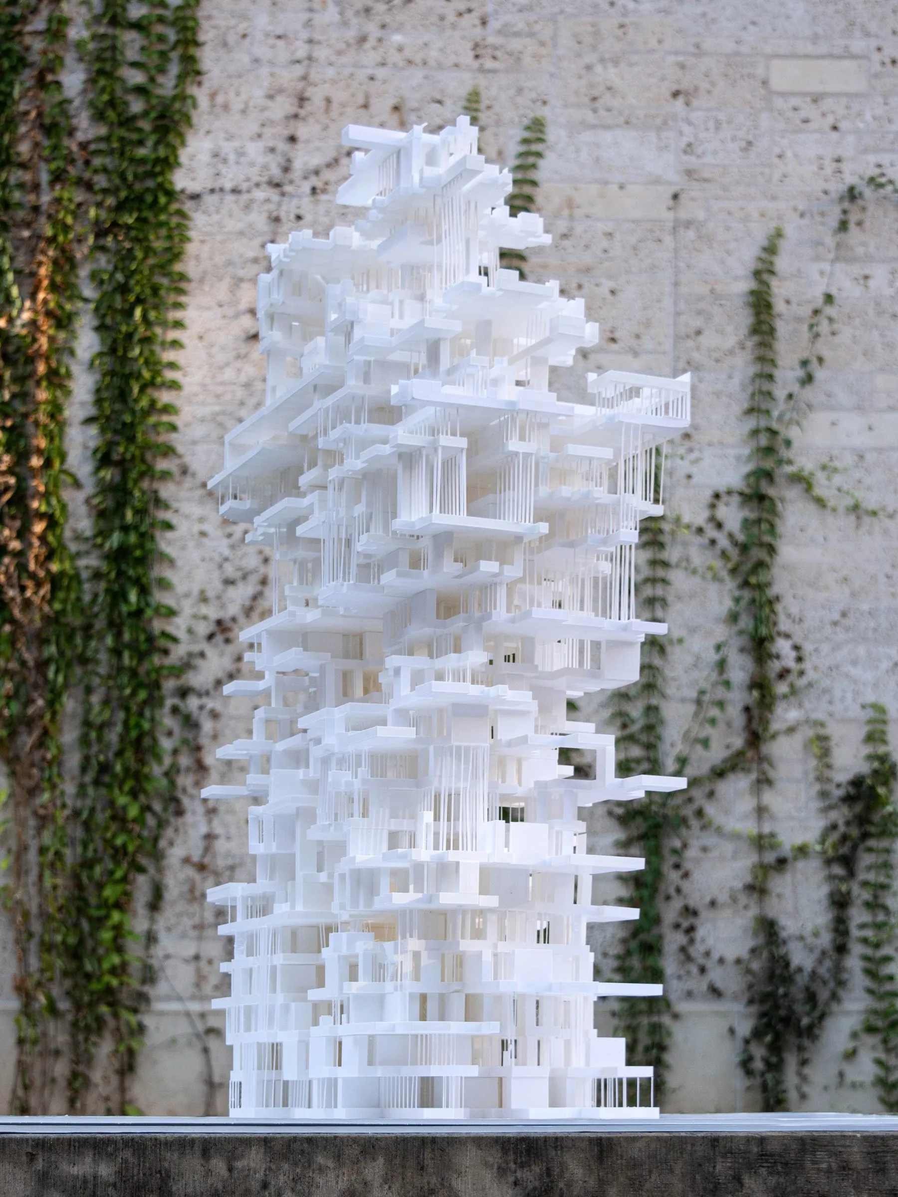A white model of stacked slabs on a wall with ivy, in daylight