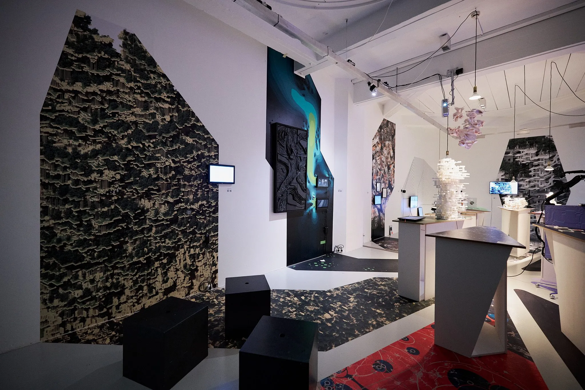 An exhibition room with dark hanging panels, screens, a red carpet and a white model on a green-topped table at its center