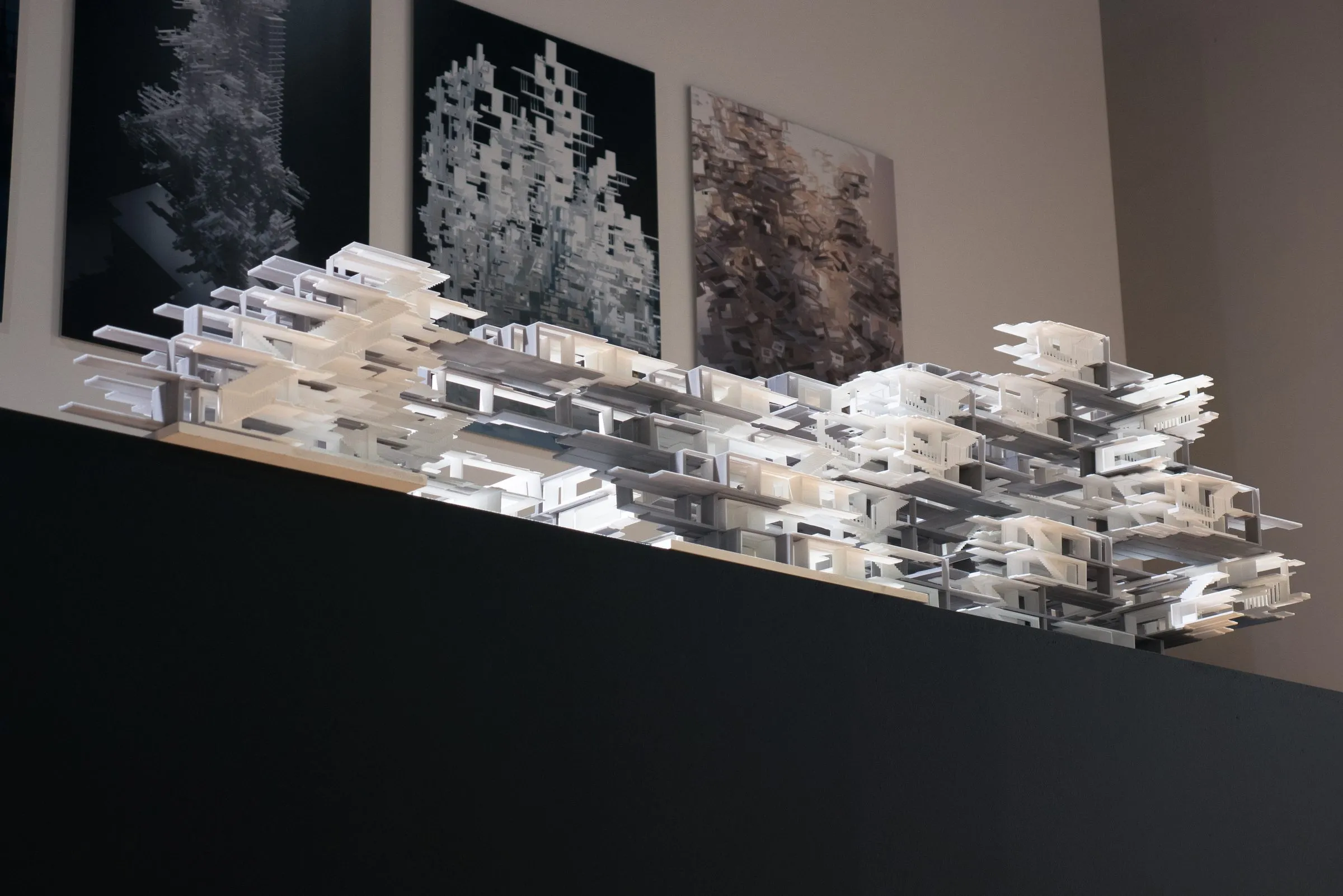 The model on the black plinth with three dark prints of aggregates on the wall behind it