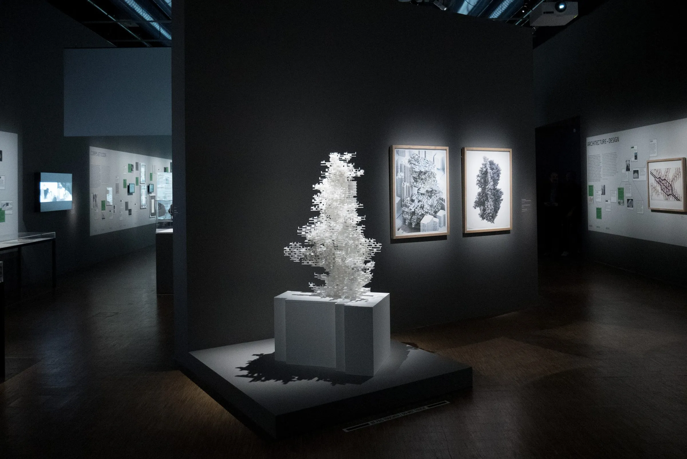 Gallery view of Coder le Monde with the WanderYards model on a plinth among framed works on dark walls