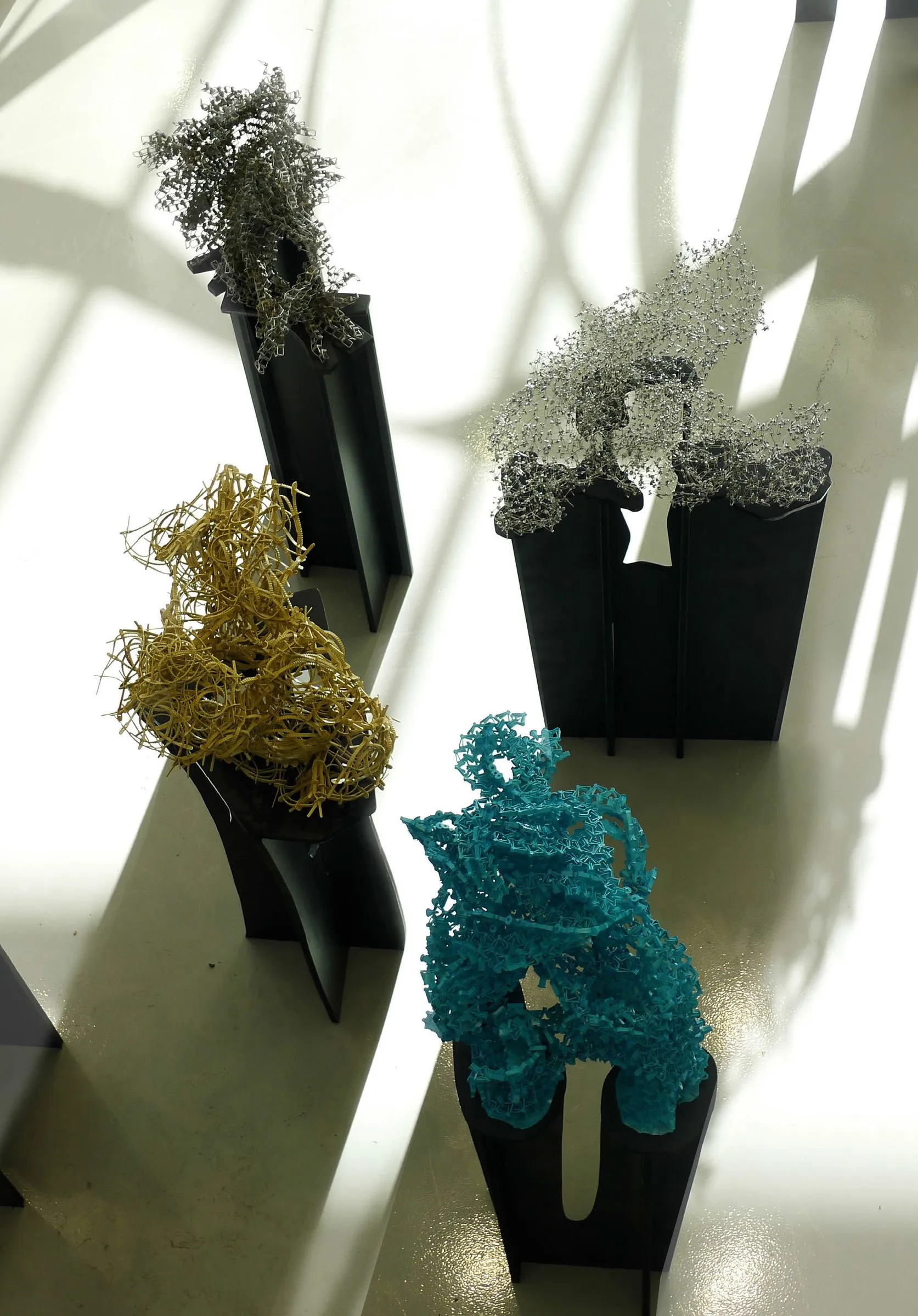 Student aggregates in yellow, white and blue on black plinths in daylight