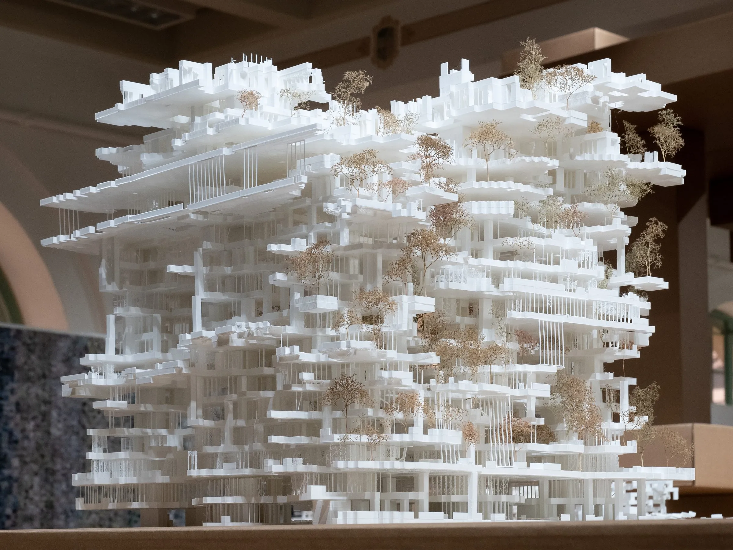 The white tower model seen from the side, its slabs cantilevering over columns and trees