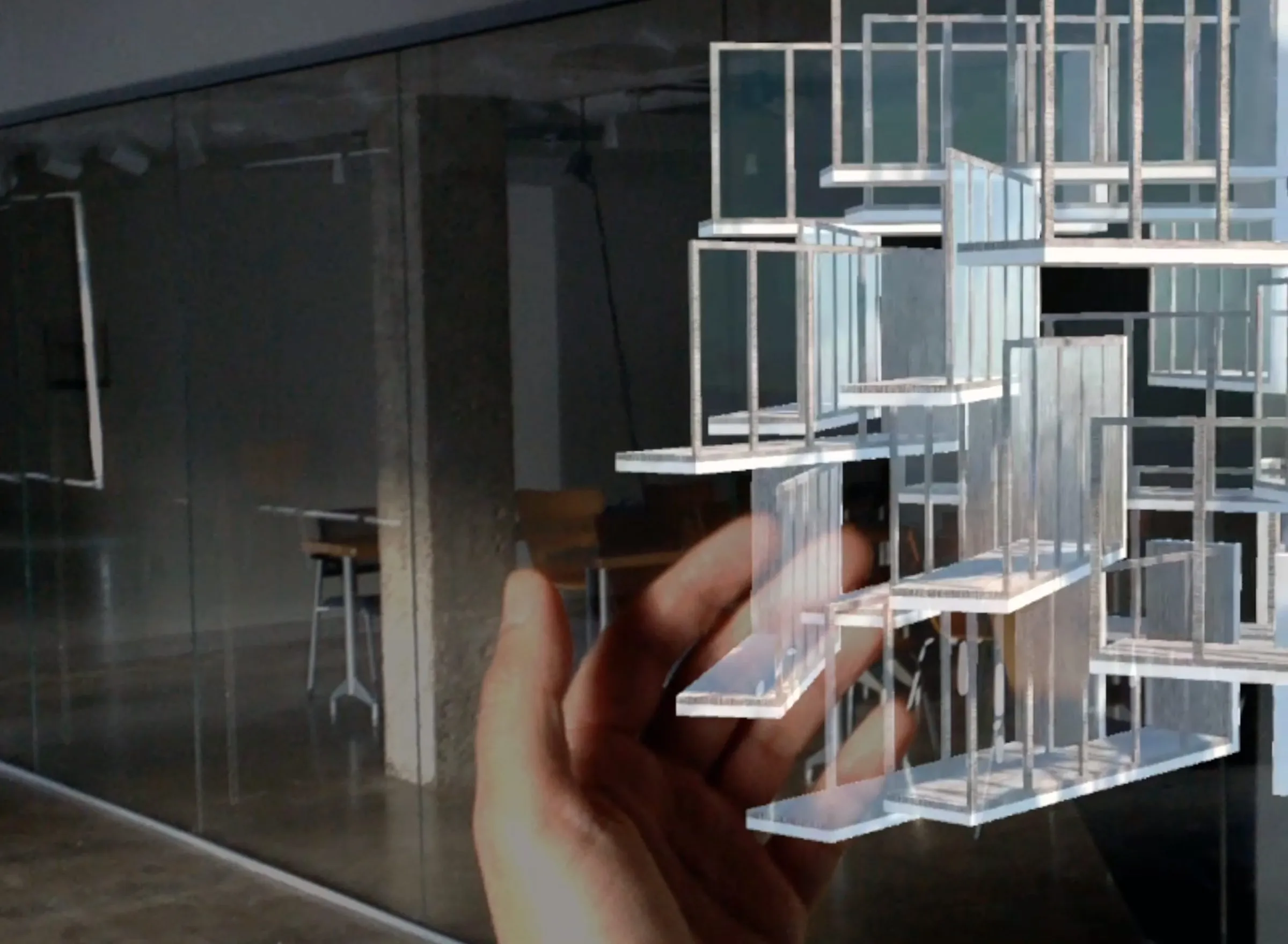 A hand holds a translucent slab element in front of a floating assembly of glass-like slabs and frames in a studio