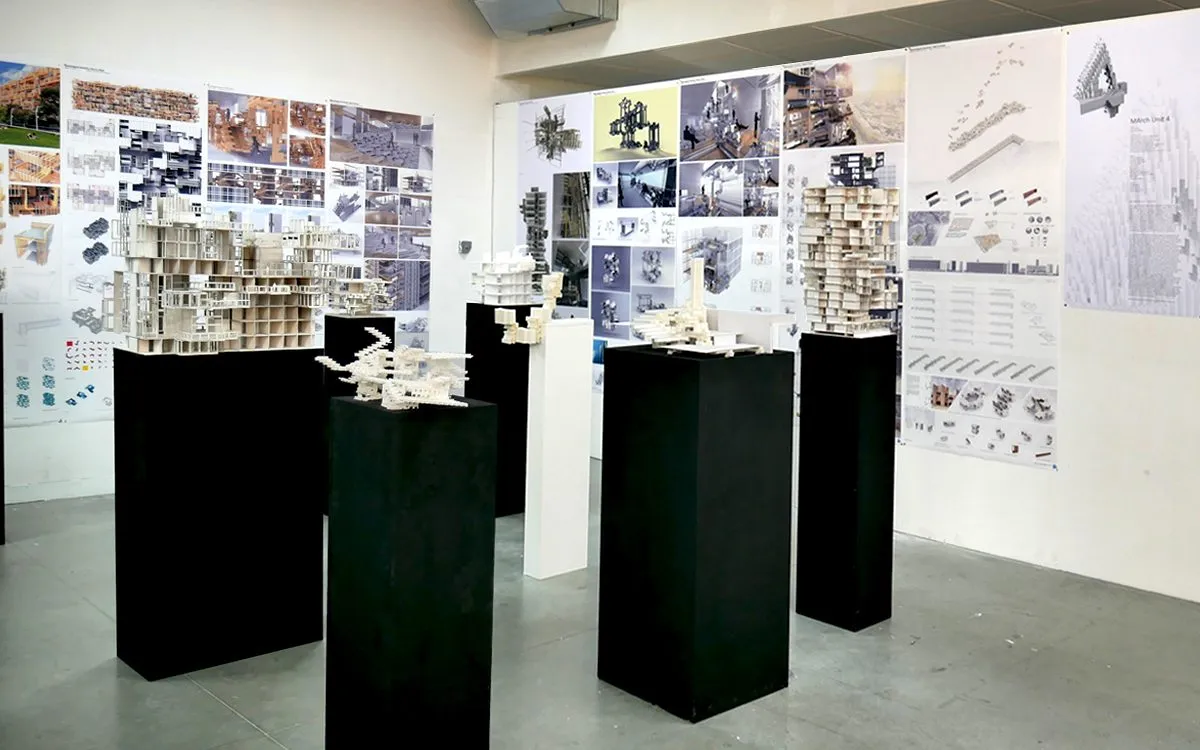 Exhibition room with student models on black plinths and drawings pinned to the walls